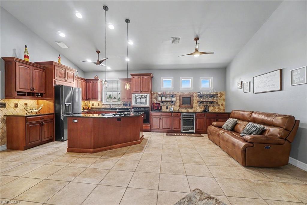 Spacious kitchen featuring warm wood cabinetry, stainless steel appliances, a central island with a dark countertop, and tile flooring