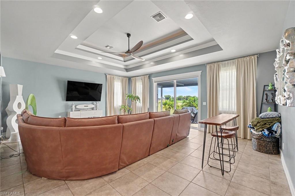 Living area featuring tile flooring, a tiered tray ceiling with recessed lighting and a ceiling fan, and sliding glass doors opening to the outdoors