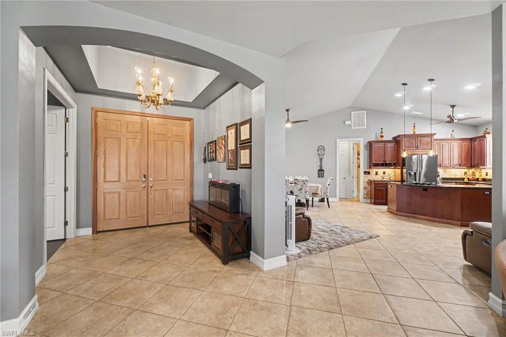 Expansive entryway featuring double paneled doors and a tray ceiling with a chandelier