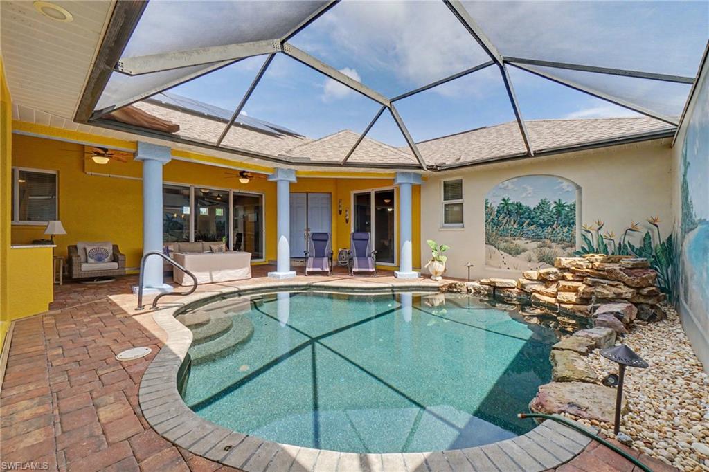 Screen-enclosed pool area featuring a freeform swimming pool with integrated steps, a rock waterfall feature, and a paved patio