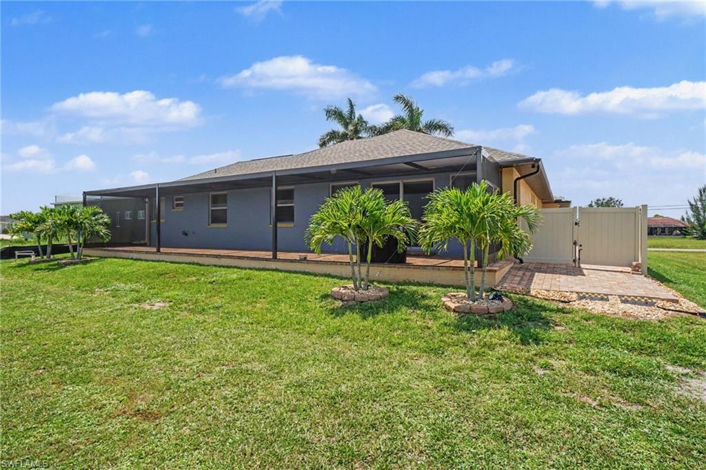 Rear exterior featuring a screened lanai with a wood-finish floor, a large grassy area, and mature palm trees