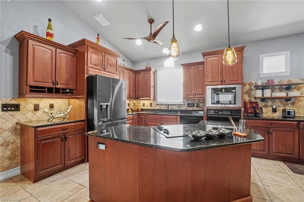 Kitchen featuring dark wood cabinetry, a central island with a cooktop, dark stone countertops, and a patterned tile backsplash