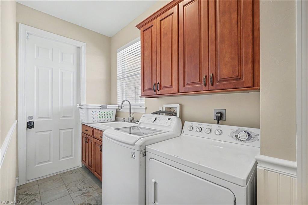 Dedicated laundry area featuring a utility sink, upper and lower wood cabinetry, and a window with blinds