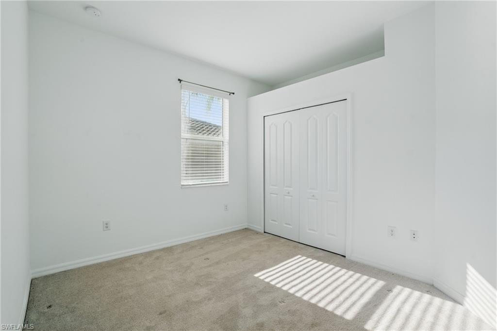 Bright bedroom with large window flooding the space with natural light, neutral carpet flooring, and a double-door closet system providing ample storage