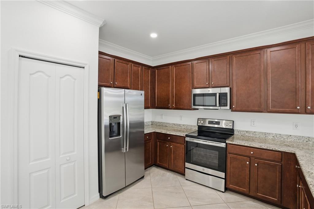 Spacious kitchen stainless steel appliances including a side-by-side refrigerator and built-in microwave, granite countertops, neutral tile flooring, and recessed ceiling lighting