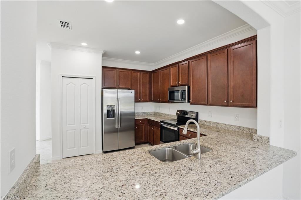 Kitchen featuring granite countertops, a stainless steel double basin sink with a gooseneck faucet, dark wood cabinetry, and stainless steel appliances including a refrigerator, microwave, and range