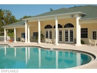 Luxurious resort-style poolscape featuring a freeform swimming pool with curved perimeter, complemented by an expansive covered loggia with classical white columns, arched transom windows, and French doors opening to the pool deck