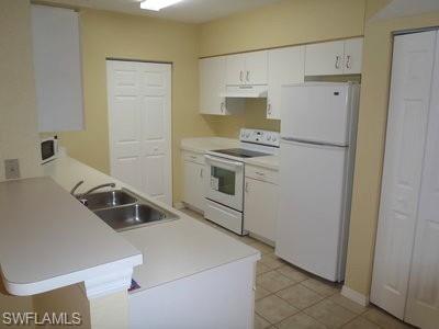 Galley-style kitchen featuring white cabinetry with chrome hardware, stainless steel appliances including a smooth-top electric range and refrigerator, stainless steel double sink with single-lever faucet, and tile flooring