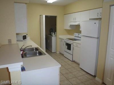 Galley-style kitchen featuring white cabinetry, tile flooring, and stainless steel appliances including a refrigerator, electric range, and microwave