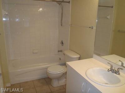 Bathroom featuring a full tub with shower, white tile surround, toilet, and a vanity with an integrated sink