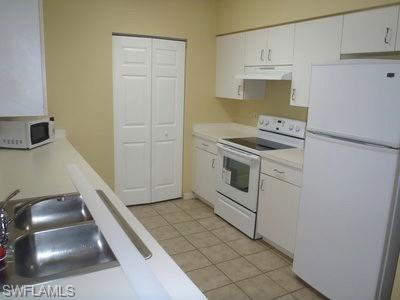 Kitchen featuring white cabinetry, light countertops, a double basin stainless steel sink with a chrome faucet, full-size white appliances, and tile flooring