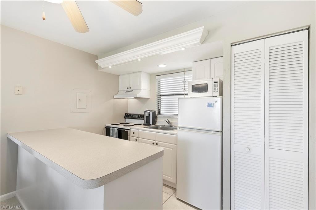 Kitchen featuring white appliances, sink, white cabinets, and ceiling fan
