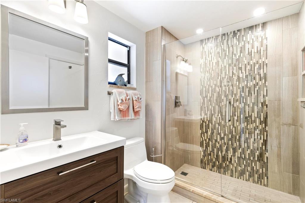 Bathroom featuring a shower with door, large vanity, and toilet