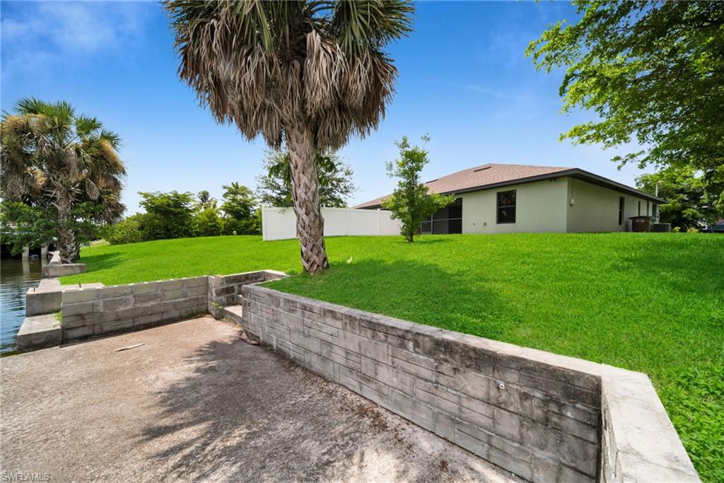 Expansive backyard featuring a manicured lawn, mature palm trees, and a concrete retaining wall with steps descending to the water