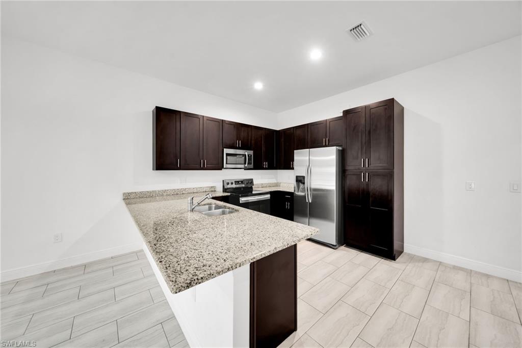 Kitchen featuring dark wood cabinetry, light-toned countertops, stainless steel appliances, and wood-finish tile flooring