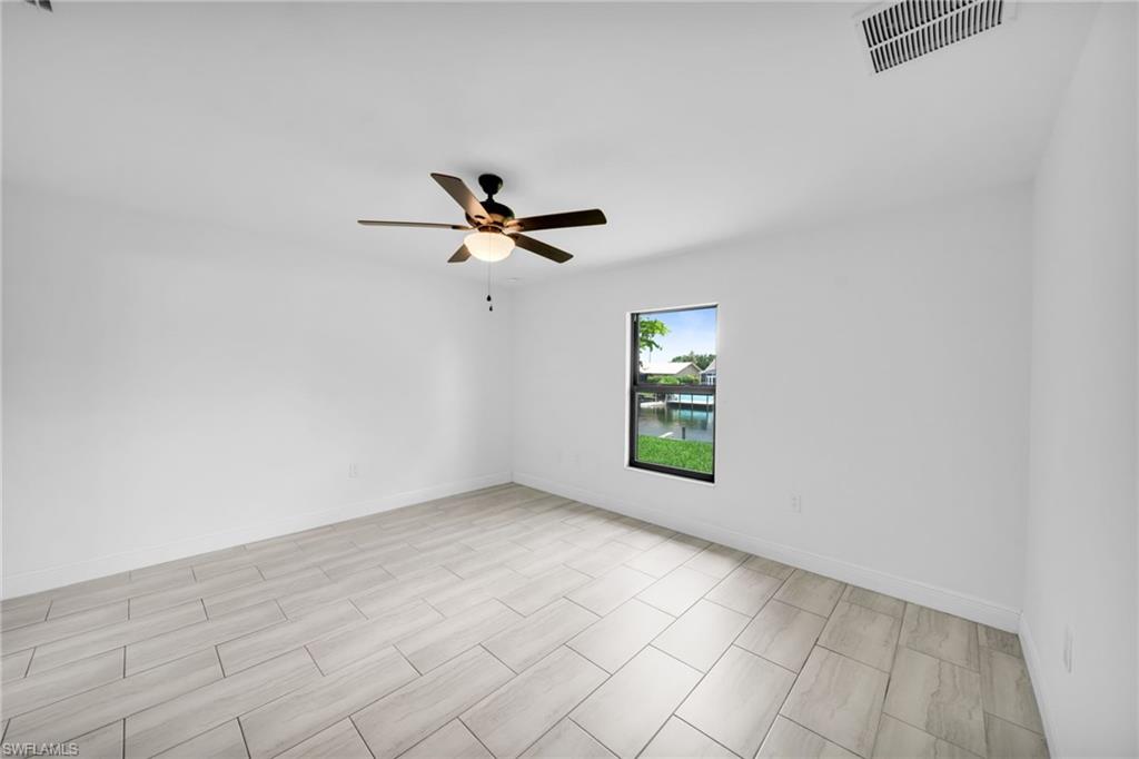 Spacious room featuring light-toned tile flooring, a dark-toned ceiling fan with integrated lighting, and a window framing a canal and distant properties
