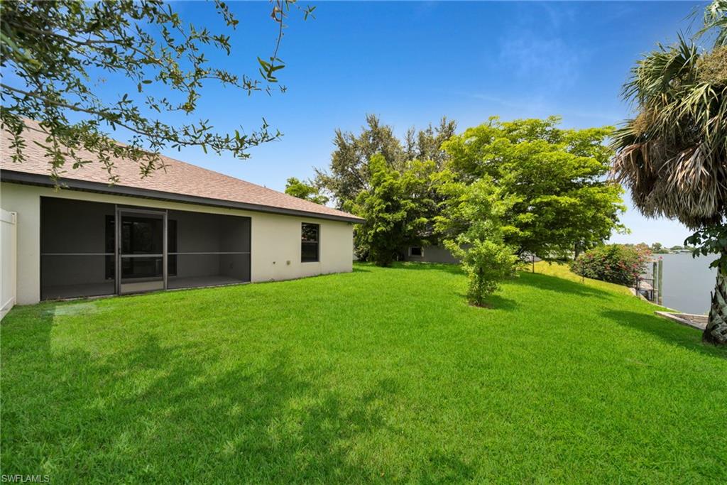 Expansive green lawn with a screened-in patio, mature trees, and waterfront access featuring a private dock