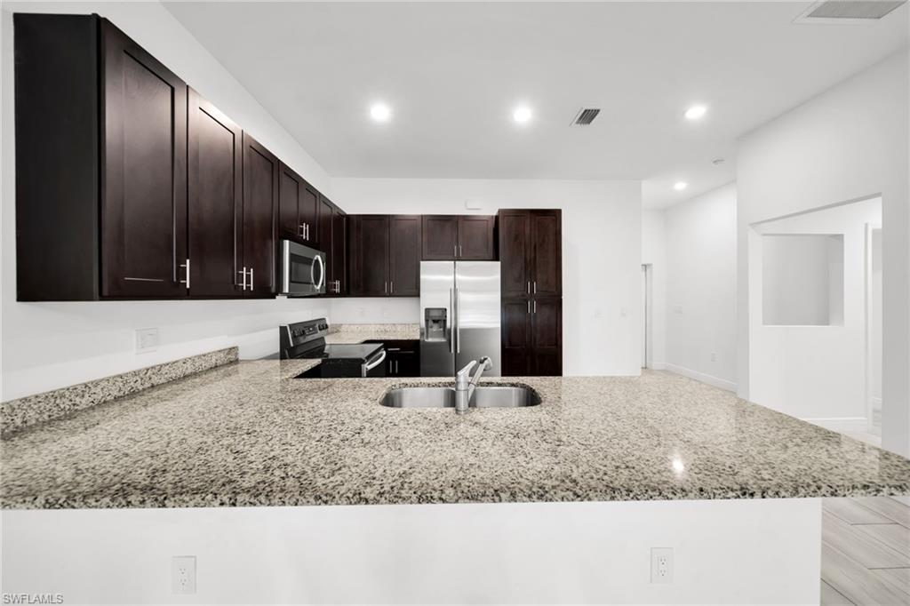 Kitchen featuring dark wood-finish cabinetry, stainless steel appliances, a double basin sink, and ample counter space with speckled light-toned countertops