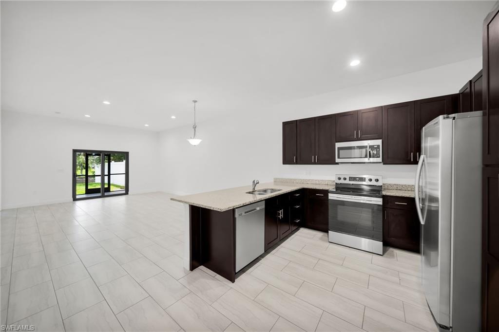 Open-concept kitchen featuring espresso cabinetry, light-toned countertops, and stainless steel appliances