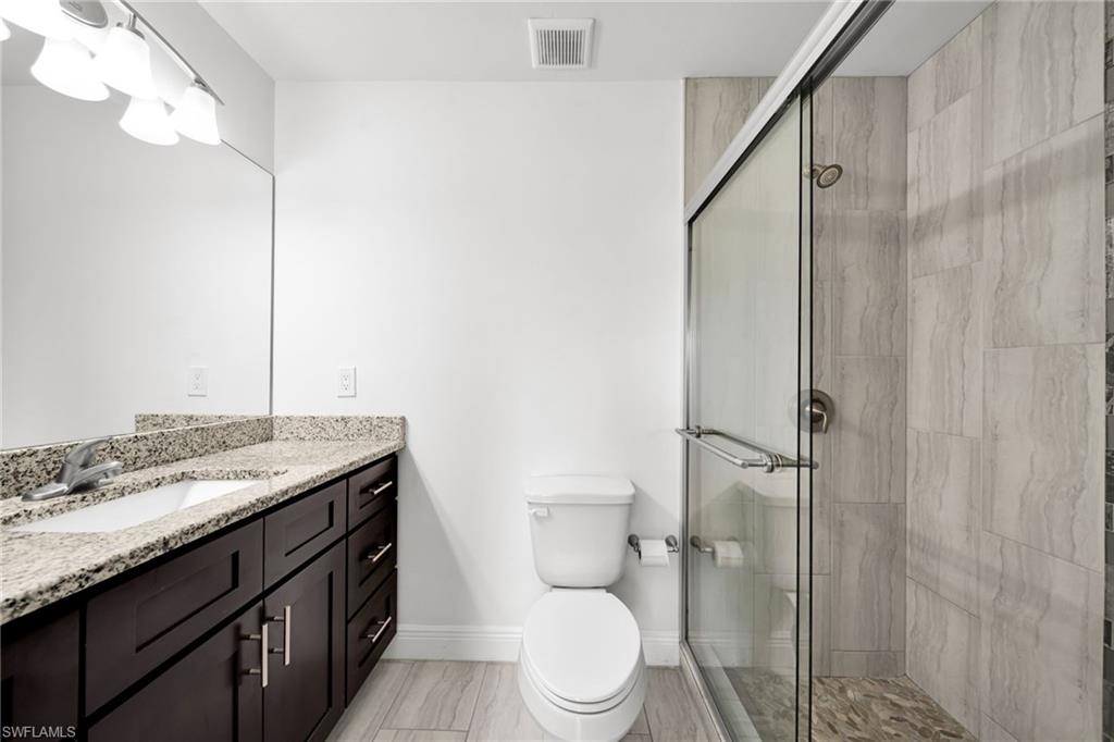 Bathroom featuring a glass-enclosed shower with tile surround and pebble flooring, a single vanity with stone countertop, and wood-finish cabinetry