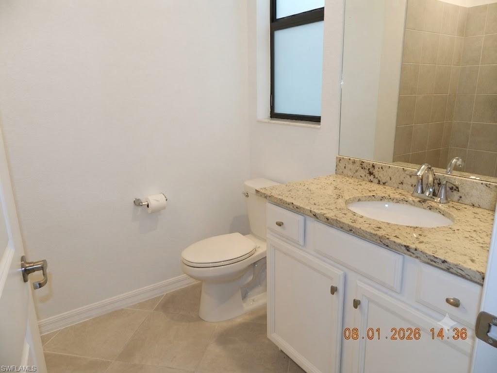 Bright and functional bathroom featuring a white ceramic toilet, white cabinetry with hardware accents, and a granite-topped vanity with an integrated sink