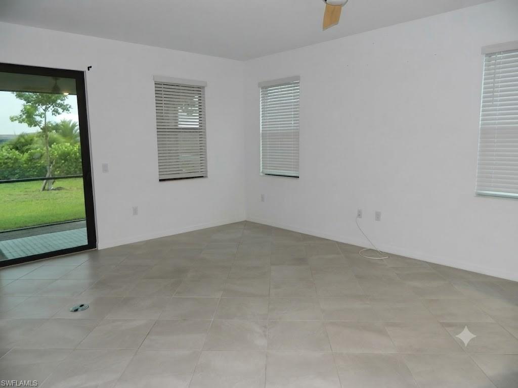 Spacious room featuring light-toned tile flooring, white walls, and a ceiling fan