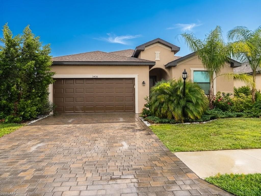 Single-story residence featuring a tan stucco exterior, a dark brown garage door, and a paver driveway