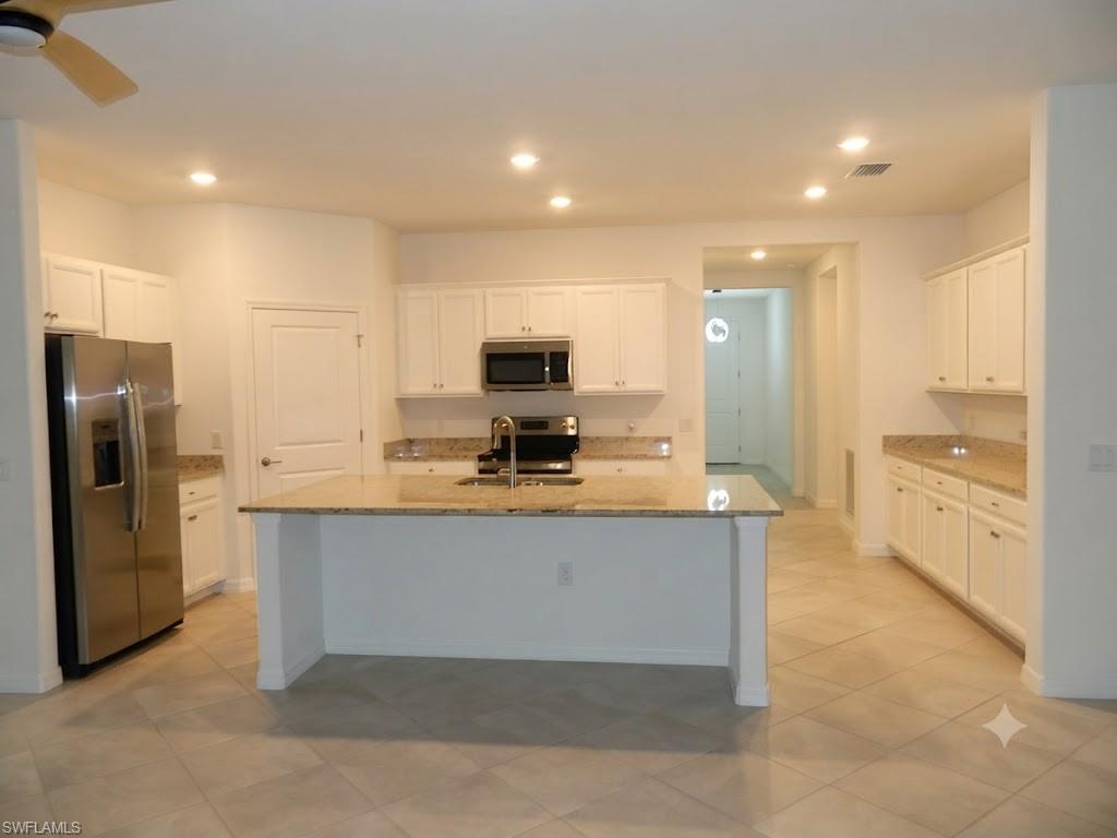 Expansive kitchen featuring a large central island, full suite of stainless steel appliances, abundant white cabinetry, light-toned countertops, and recessed lighting