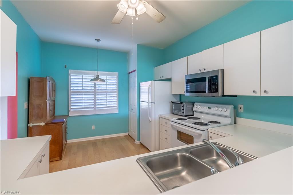 Kitchen featuring white cabinetry, stainless steel microwave, white appliances, and light wood-finish flooring