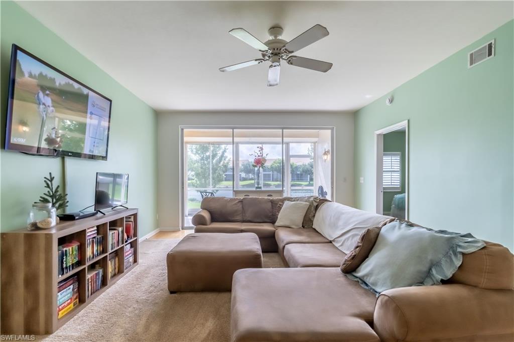 Wall-mounted television with a wood-finish media console, overhead ceiling fan with light fixture, and sliding glass doors leading to an outdoor area