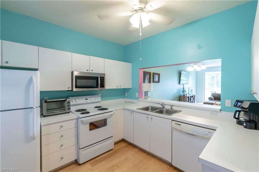Kitchen featuring white cabinetry, white appliances, a stainless steel microwave, light-toned flooring, and a pass-through window