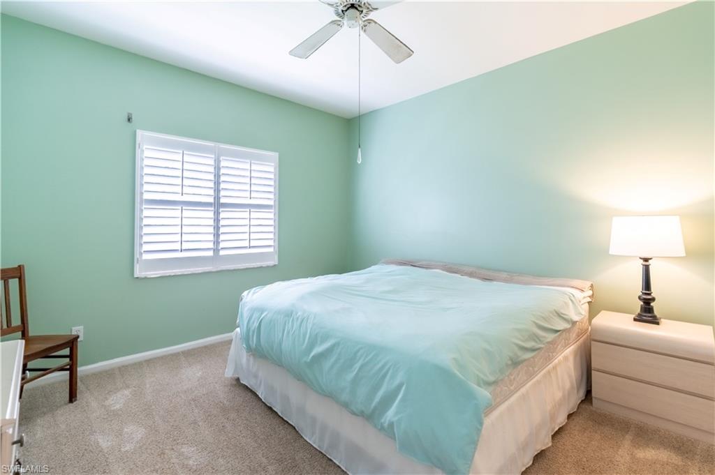 Window with white plantation shutters, ceiling fan, and light-toned carpet flooring