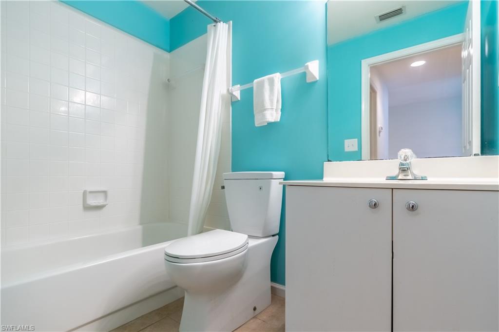 White bathtub with tiled surround, white toilet, white vanity with cabinet storage, and wall-mounted mirror