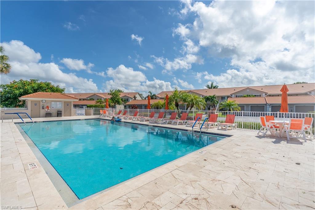 Outdoor swimming pool with integrated steps, surrounded by a light-toned paved deck, a white picket fence, and a pool house with a terracotta-style roof