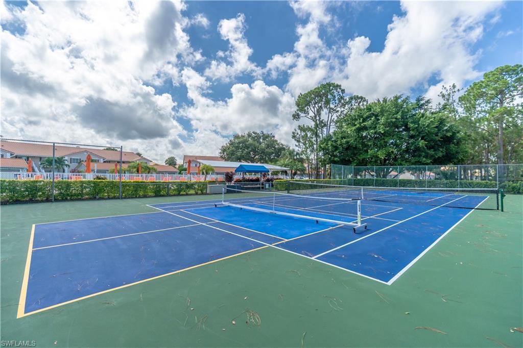 Two well-maintained tennis courts with blue playing surfaces and green surrounds, bordered by lush landscaping and mature trees