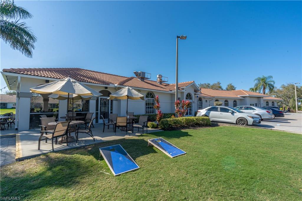 Tiled roof exterior with arched windows, expansive patio area with built-in string lighting, manicured green space, and a paved parking area