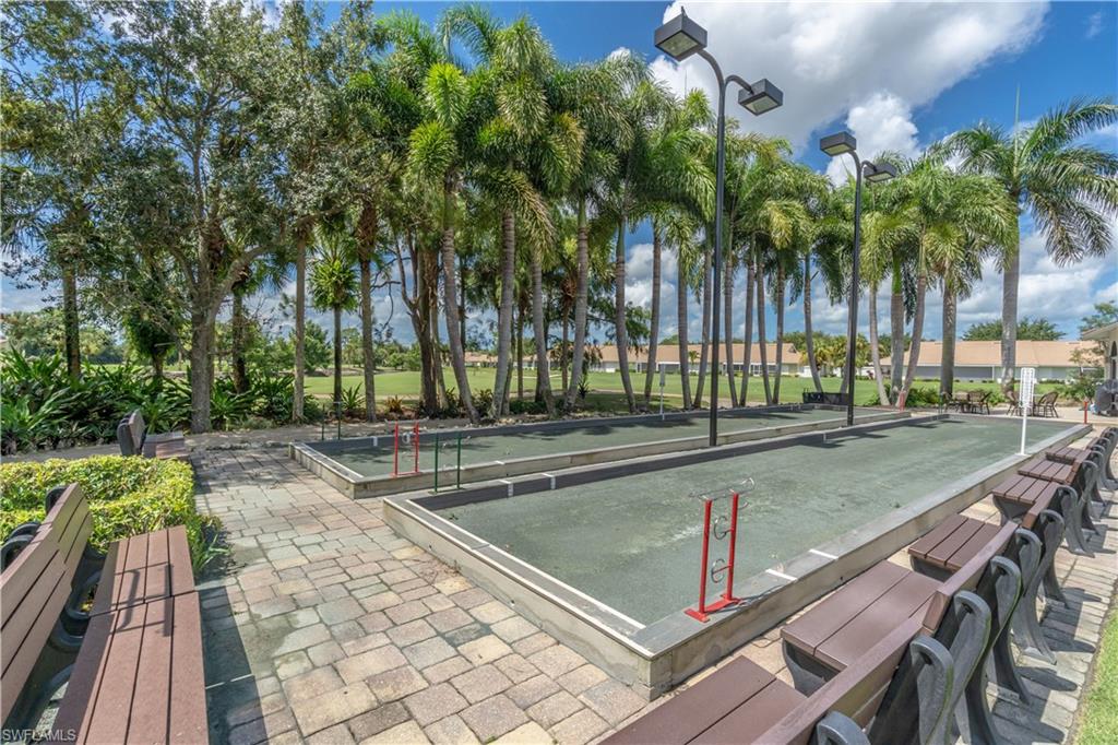 Bocce ball court with surrounding benches, paved walkway, mature palm trees, and overhead lighting