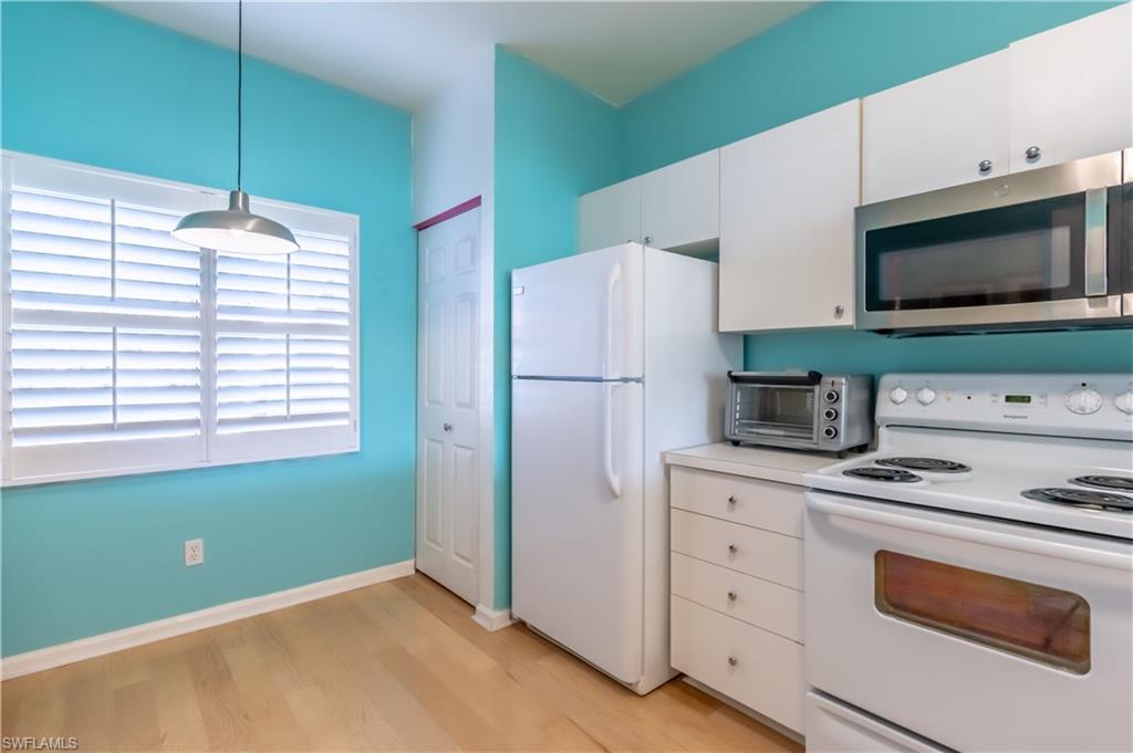 Kitchenette featuring wood-finish flooring, white cabinetry, stainless steel microwave, and plantation shutters