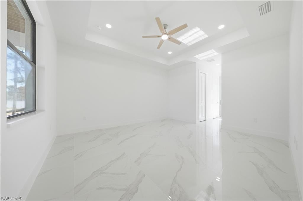 Recessed lighting, ceiling fan, white tray ceiling, white tile flooring, and a large window