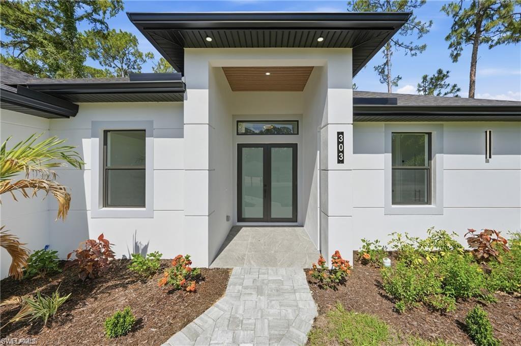 Modern architectural facade with a covered entry, wood-finish ceiling accent, double glass entry doors, and a paver walkway