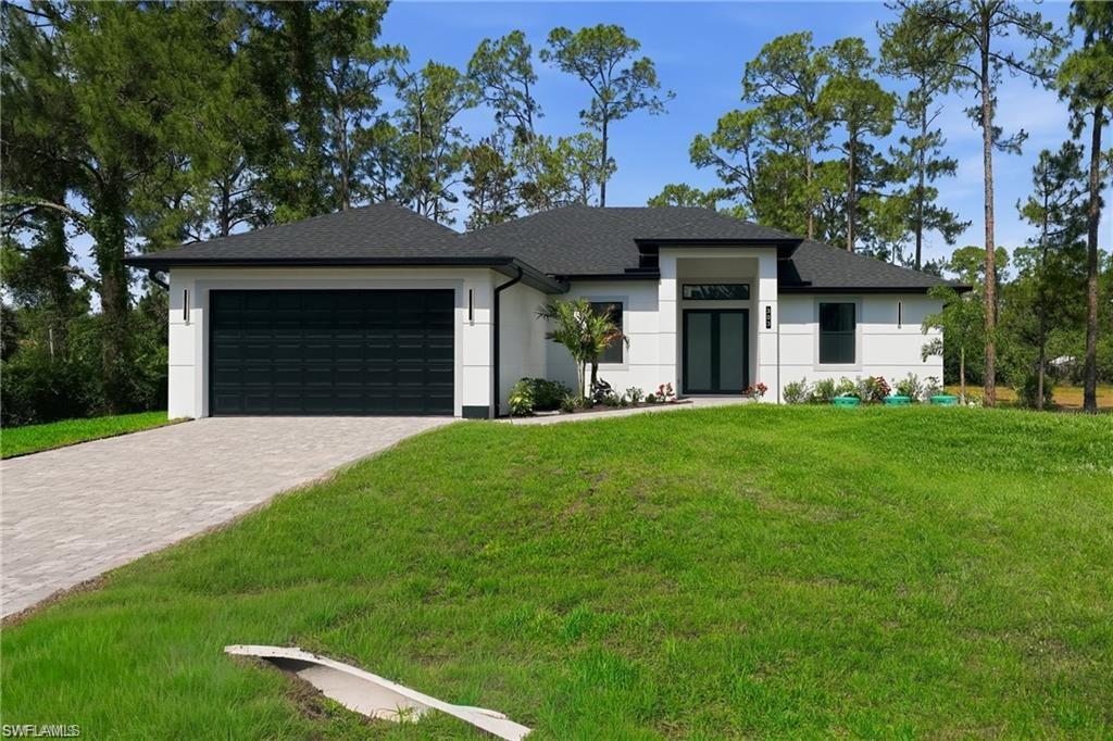 Modern residence featuring a clean-lined white exterior with dark roof accents, two-car garage with horizontal panel detailing, and a wide paver driveway