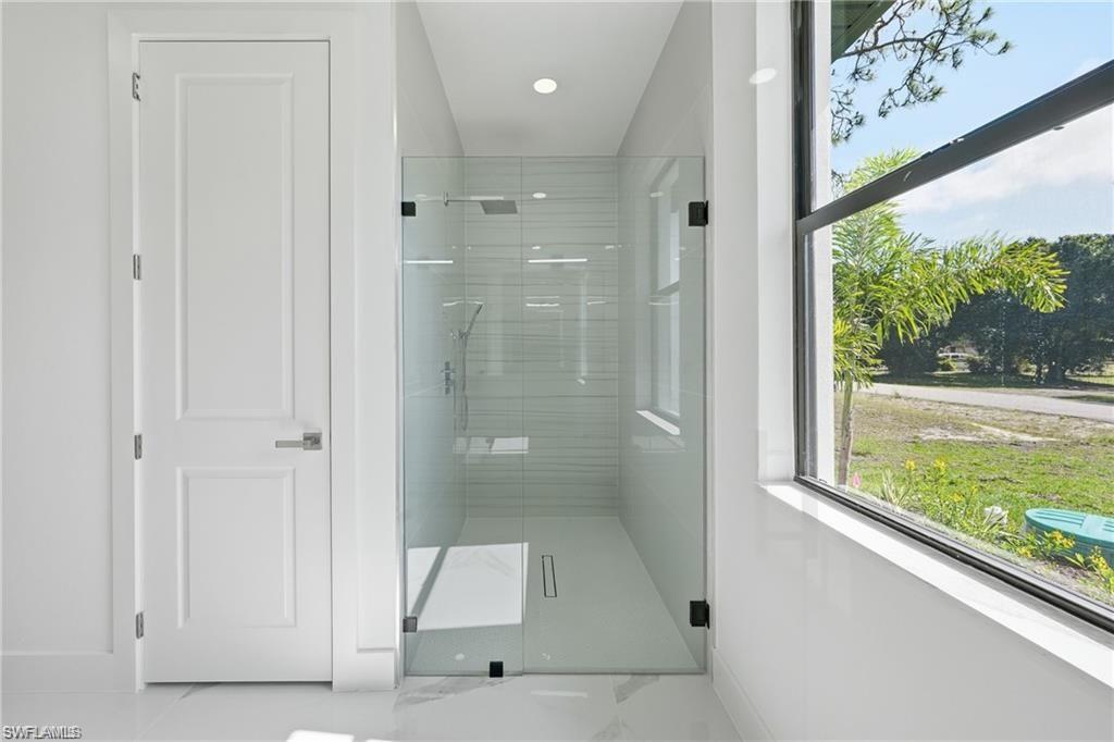 Frameless glass shower enclosure with a rainfall showerhead, white tiled walls, and a linear drain