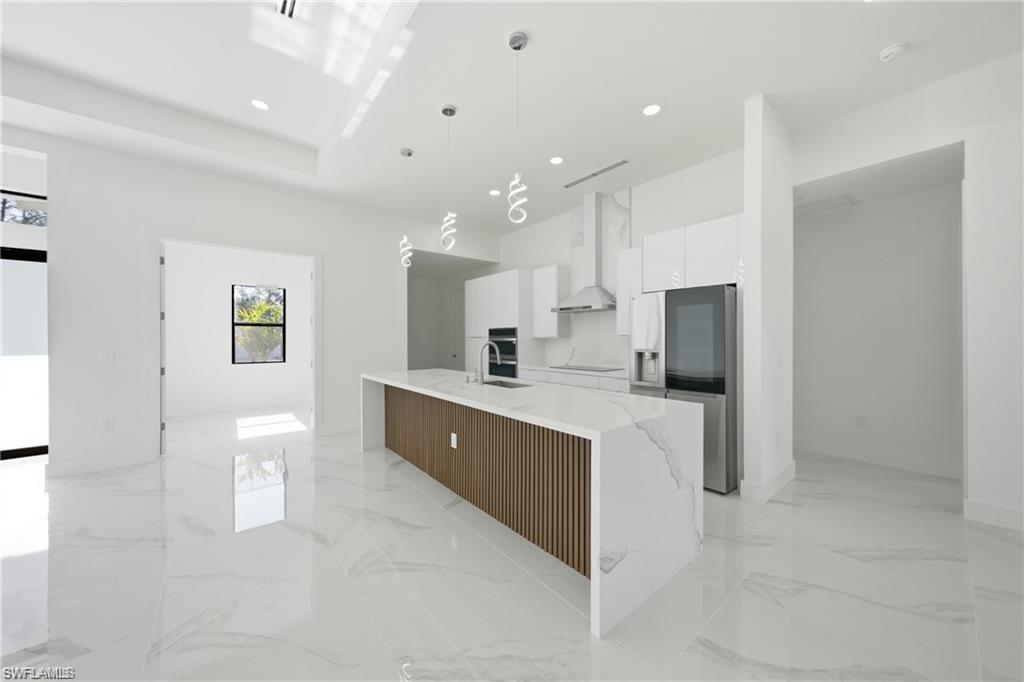 Gourmet kitchen with a waterfall island, integrated stainless steel appliances, white gloss cabinetry, and recessed lighting