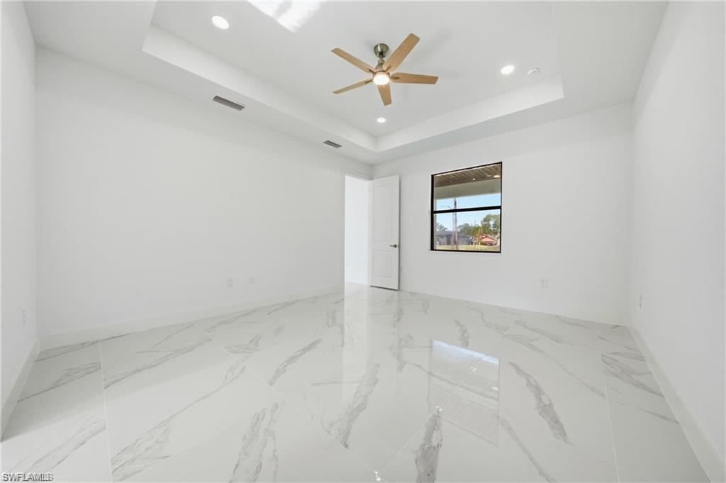Tray ceiling with recessed lighting, ceiling fan, large window, and white tile flooring
