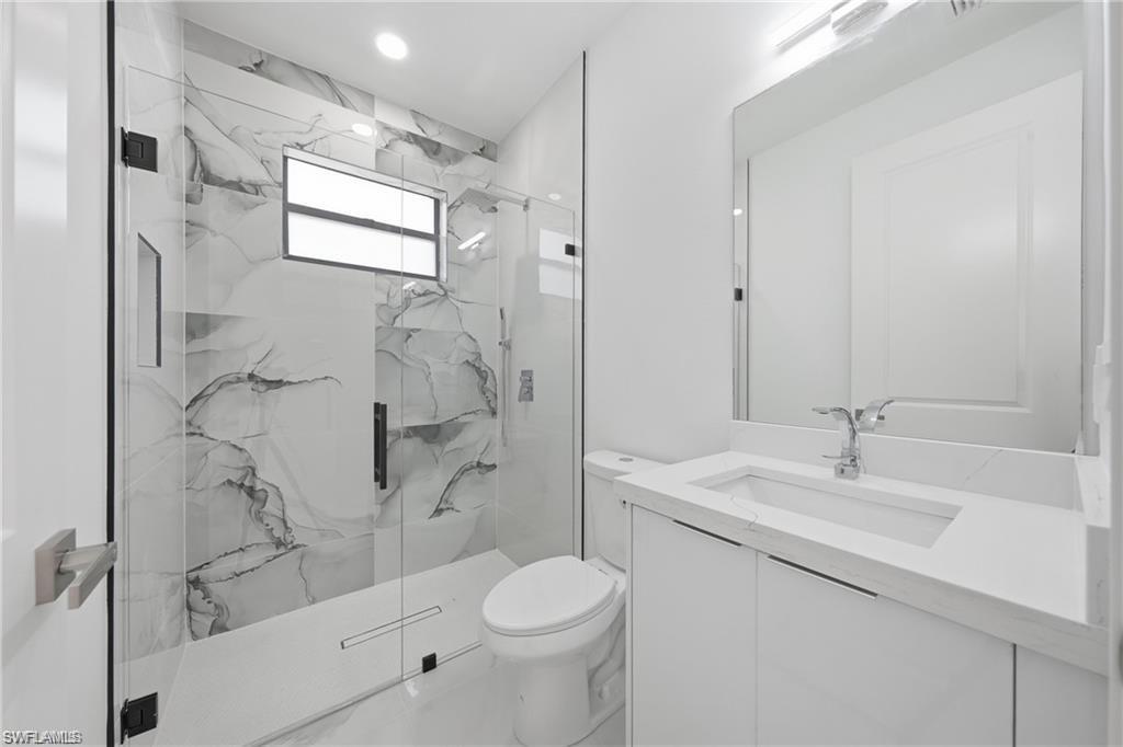Modern bathroom featuring a frameless glass shower enclosure, large format marble-look tile, a built-in shower niche, a window, and a vanity with an integrated sink