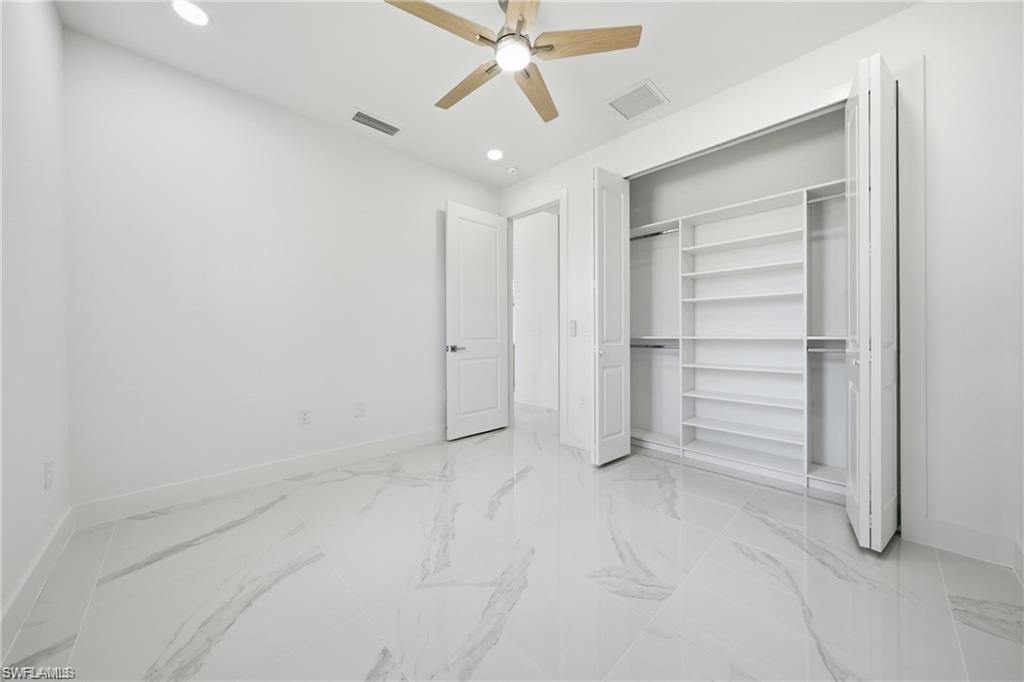 White porcelain tile flooring with gray veining, recessed ceiling lighting, ceiling fan with wood-finish blades, white walls, and a built-in closet organization system