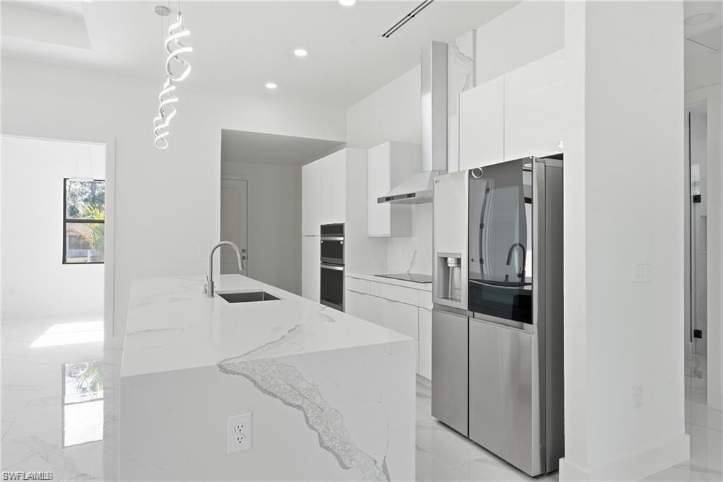 Kitchen featuring a waterfall-edge island with an undermount sink, stainless steel appliances, white cabinetry, and a modern pendant light fixture