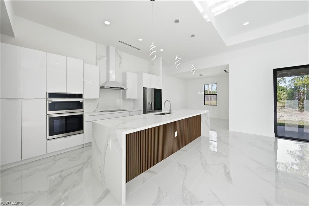 Gourmet kitchen featuring a waterfall island, integrated stainless steel appliances, gloss white cabinetry, and marble-patterned flooring
