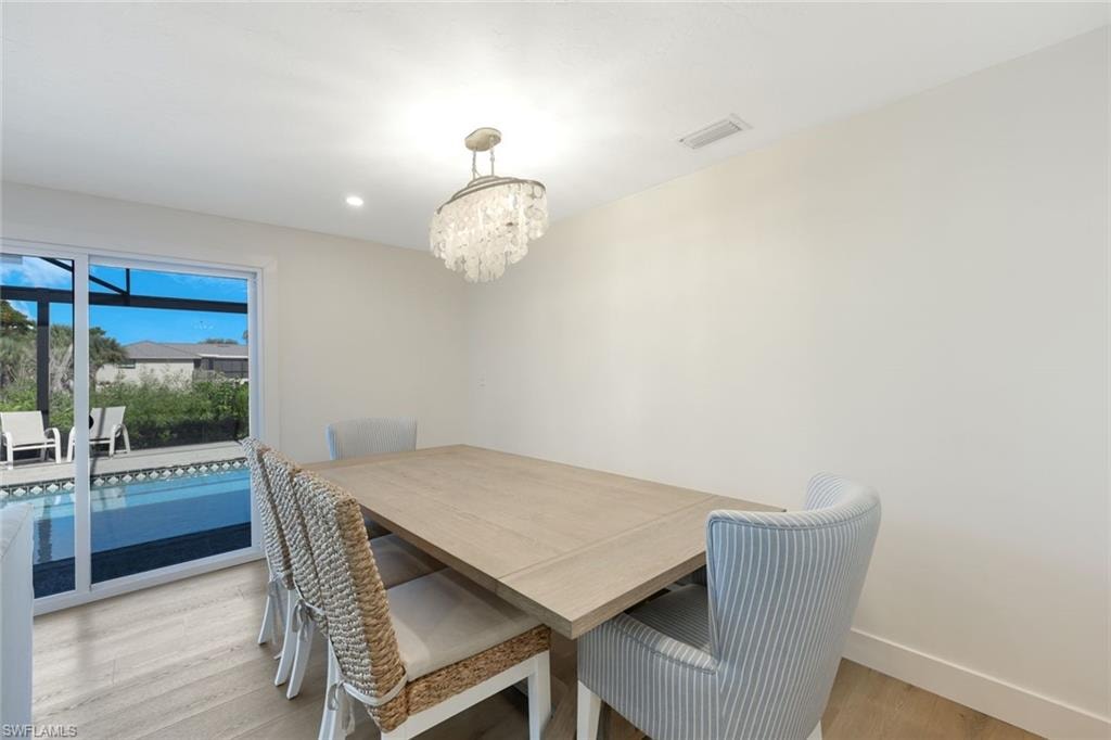 Dining area with light wood-finish flooring, a crystal chandelier, and bright white walls