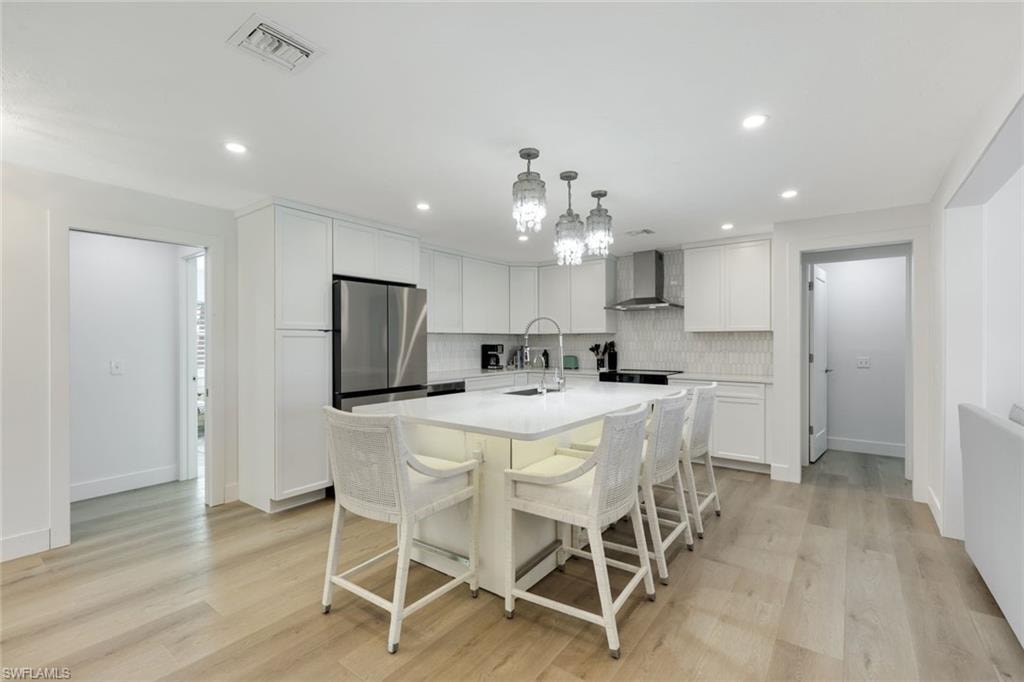 Modern kitchen featuring white cabinetry, a large waterfall-edge island with seating for four, stainless steel appliances, and pendant lighting